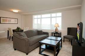 A living room with a grey couch, a black coffee table, and a flat screen TV at Dominion Towers Apartments, Arlington, VA