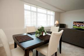 A modern dining room with a wooden table and white chairs at Dominion Towers Apartments, Arlington, VA, 22204