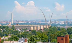 A cityscape with a large building in the background and a plane flying in the sky at Dominion Towers Apartments, Arlington, Virginia