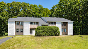 A white house with a grey roof and a green lawn in front.