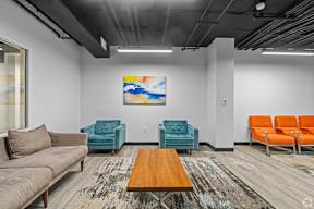 A room with a painting on the wall and a couch, chair, and table.