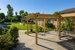 A wooden pergola with a white ball on top is situated in a sunny backyard with a picnic table and a paved patio.