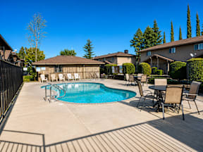 A pool surrounded by chairs and a table with a house in the background.