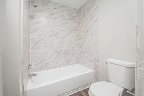 A white bathroom with a marble tile wall.
