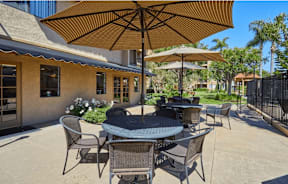 a patio with tables and umbrellas in front of a building at Huntington Terrace North Senior, Huntington Beach, CA