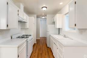 A white kitchen with wood floors and white appliances.