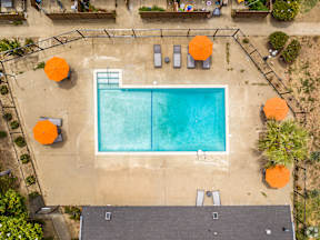 An aerial view of a swimming pool surrounded by orange umbrellas and lounge chairs.