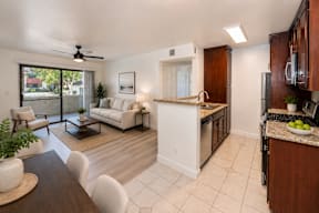 A modern kitchen and living room with white furniture and a ceiling fan.