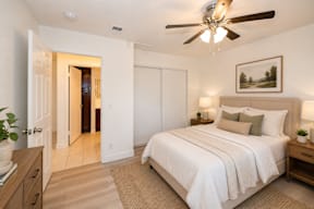 A bedroom with a large bed, a ceiling fan, and a painting on the wall.