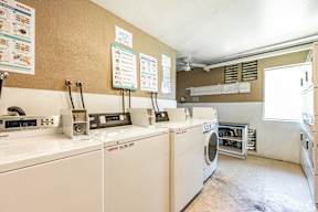 A laundromat with washers and dryers and signs on the wall.