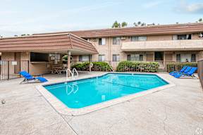 A swimming pool in front of a building with a red tiled roof.