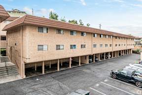 A parking lot in front of a tan building with a brown roof.