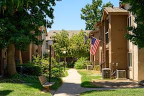 a pathway with a bench and trash cans in front of an apartment building at Oak Terrace Senior Apts, California, 92543