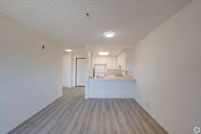 an empty living room and kitchen with white walls and wood floors at Flamingo Garden Senior Apts, El Monte