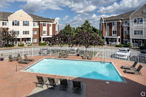 A swimming pool surrounded by chairs and trees in front of apartment buildings.