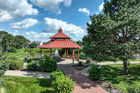 A gazebo is surrounded by greenery and a brick walkway.