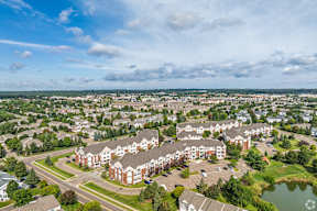 A large apartment complex with a pond in the foreground and a cloudy sky above.