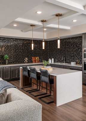 A modern kitchen with a white island and dark chairs.