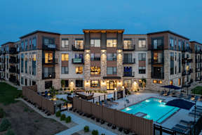 A modern apartment complex with a pool at dusk.