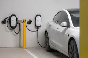 A white car is charging at a yellow charging station.