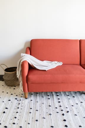 a red couch with a white blanket and a basket on the floor