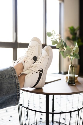 a woman holding a pair of white sneakers on a table