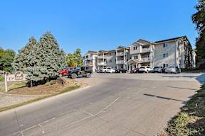 A parking lot in front of a multi-story apartment building with cars parked.
