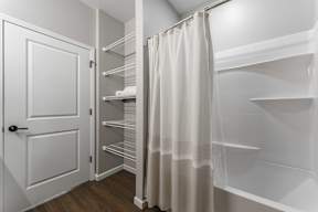 A white door opens to a walk-in closet with shelves and a curtain.