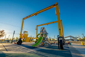 A playground with a yellow crane structure and a green slide.