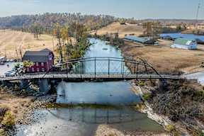 A red barn sits next to a bridge over a river.