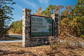 A sign for the Hobbs State Park-Conservation Area Visitor Center stands in front of a forest.