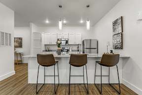 A kitchen with white cabinets and a white island with brown barstools.