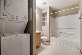 A white washing machine is in a laundry room with a toilet and a bathtub.