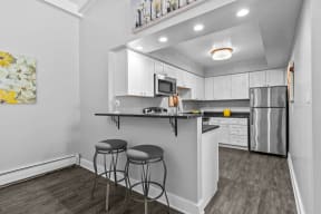 a kitchen with white cabinets and a black counter top with two stools at Apple Ridge Apartments - Livonia, MI, Livonia, 48152