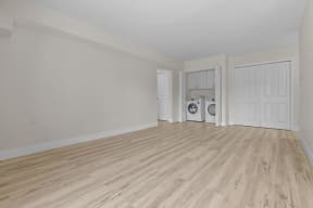 the living room and laundry room of an apartment with white walls and wood flooring