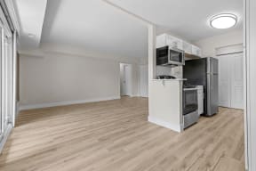 an empty living room with a kitchen with a refrigerator and a microwave