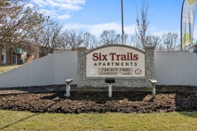 a sign for six trails apartments in front of a fence