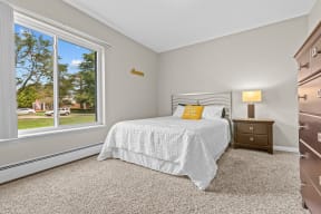 a bedroom with a bed and a dresser at Apple Ridge Apartments - Livonia, MI, Livonia, Michigan