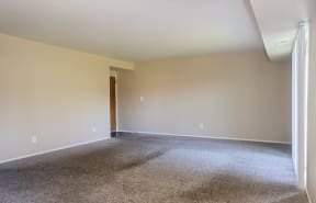 an empty living room with carpet and a door to a bedroom