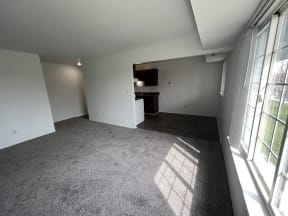 an empty room with a large window and a kitchen in the background