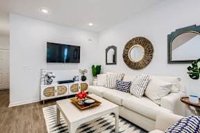 A living room with a white couch, a coffee table, and a flat-screen TV mounted on the wall.