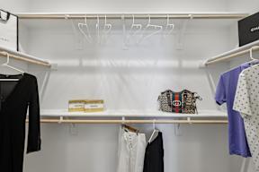 A closet with clothes hanging and a purse on the shelf.