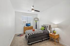 A bedroom with a bed, a ceiling fan, and a window with blinds.