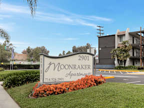 A sign for Moonraker Apartments is surrounded by flowers and greenery.
