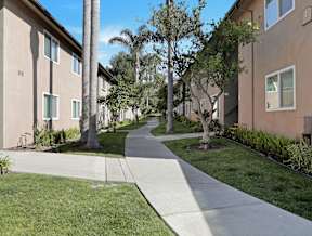 A concrete pathway leads through a grassy area between two rows of apartment buildings.