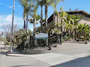 A sign for "Idylwood" stands in front of a building with a brick wall and palm trees.