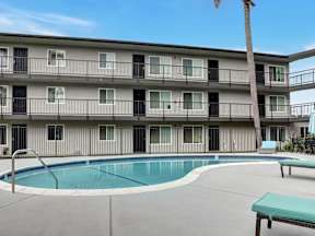 A pool is surrounded by a concrete patio and a building with balconies.