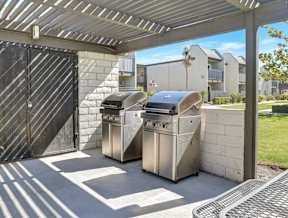 Two stainless steel barbecues are placed under a covered patio area.