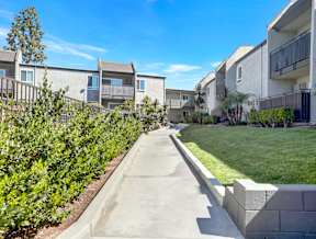 A concrete pathway leads through a well-manicured grassy area in front of apartment buildings.