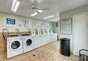 A laundry room with a row of washers and dryers and a sign on the wall.